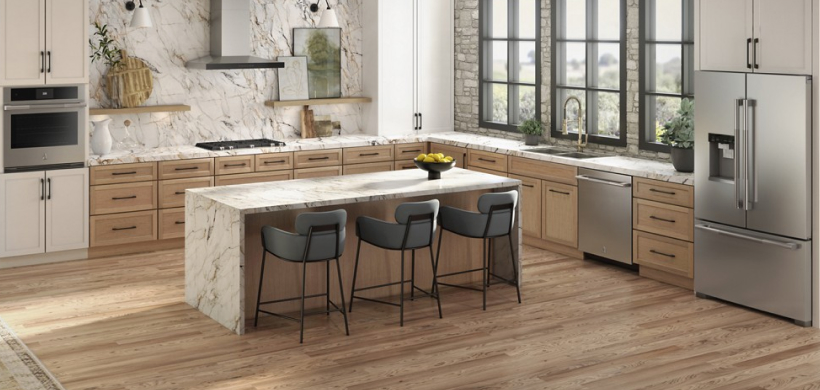 Une cuisine équipée d'un four mural JennAir, d'une table de cuisson et d'une hotte JennAir, d'un lave-vaisselle JennAir et d'un réfrigérateur JennAir. On peut voir un îlot avec trois chaises. Sur les comptoirs se trouvent une cruche en céramique, des plantes, une planche à découper et différents objets. Sur les étagères près de la table de cuisson, on voit des plantes, des planches à découper et autres objets.